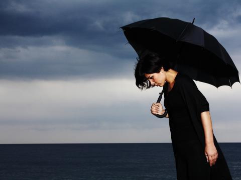 Das Bild zeigt eine Frau mit einem Regenschirm in der Hand. Über ihr ziehen dunkle Wolken auf.