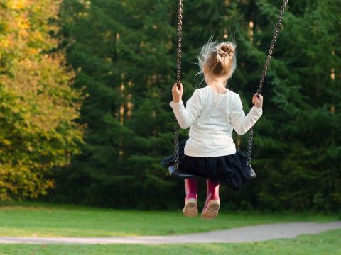 Ein schaukelndes kleines Mädchen, das mit dem Rücken zum Betrachter sitzt 